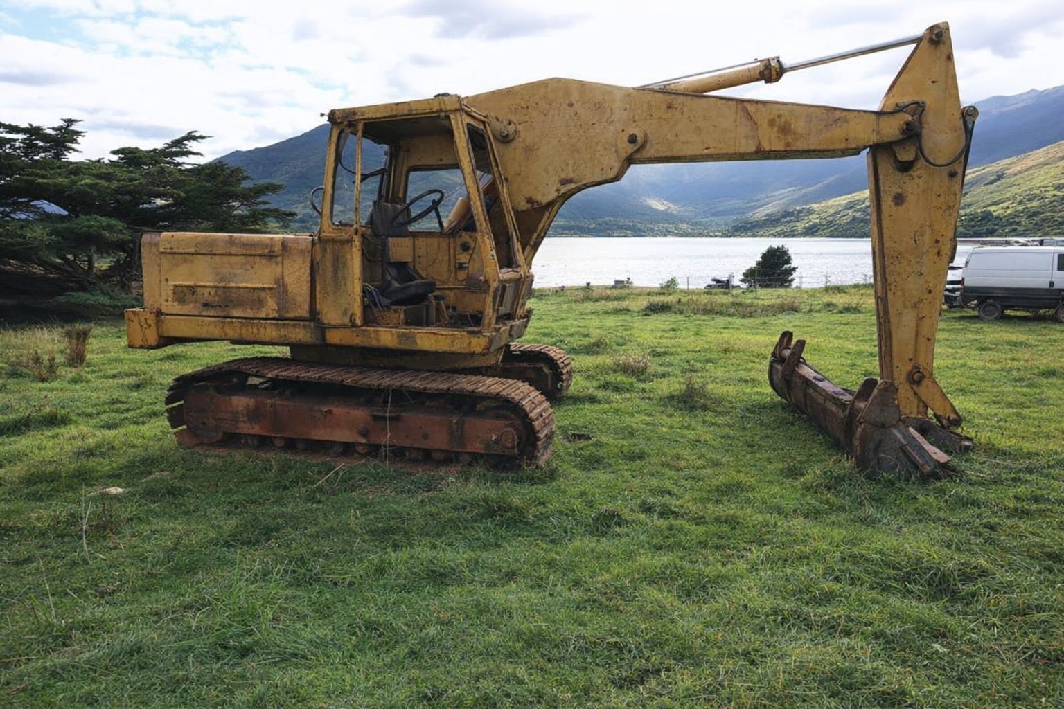 Ein alter, gelber Kettenbagger steht auf einer Wiese vor einem See.