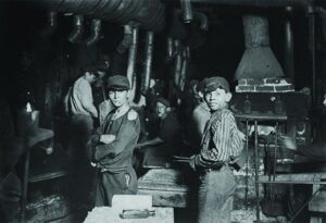 Historische Fabrikarbeiter in einer dunklen Werkstatt mit Schornstein und Maschinen