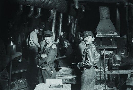 Historische Fabrikarbeiter in einer dunklen Werkstatt mit Schornstein und Maschinen